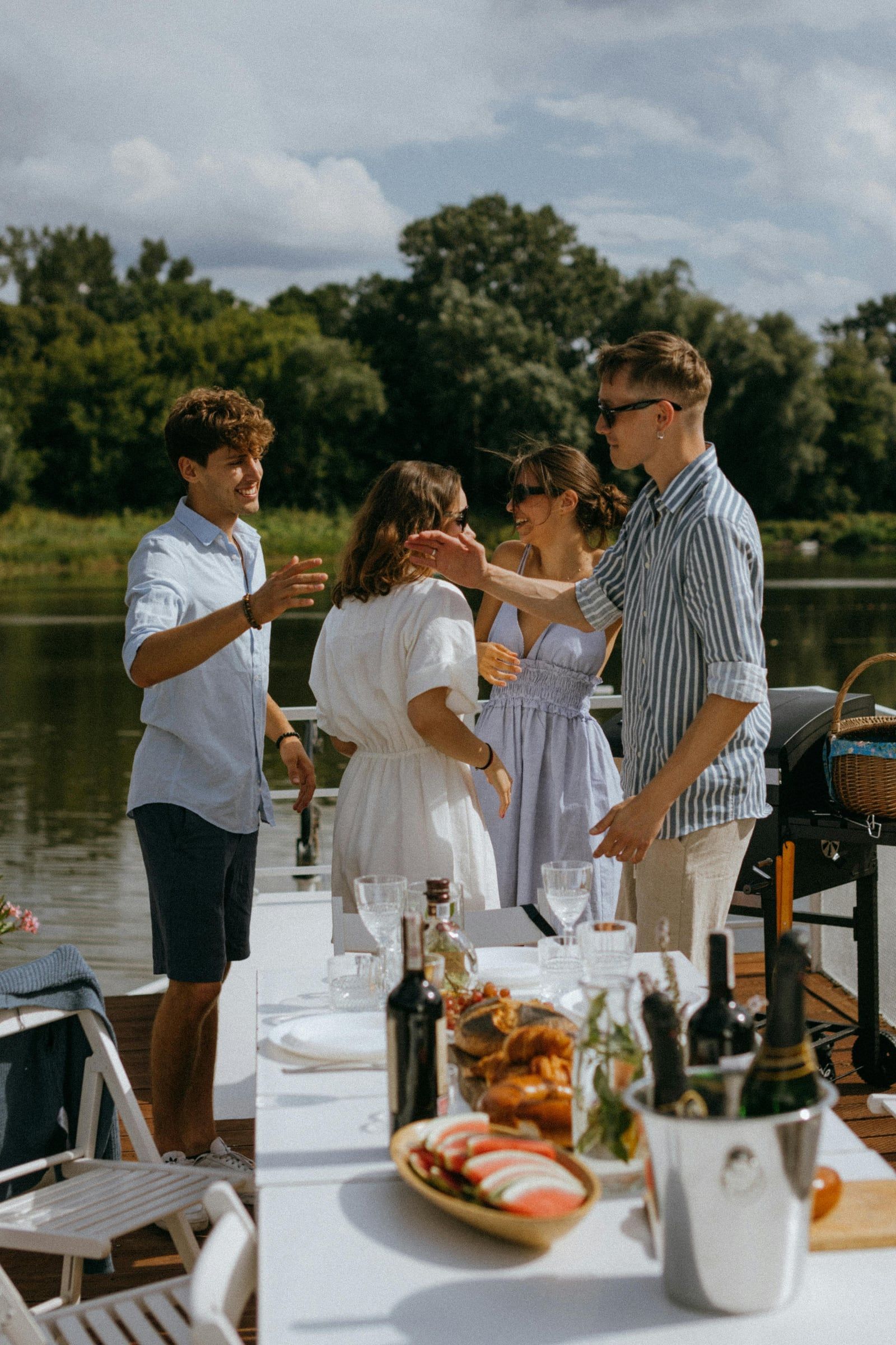 Friends laughing around a table of food and drinks on a boat deck.